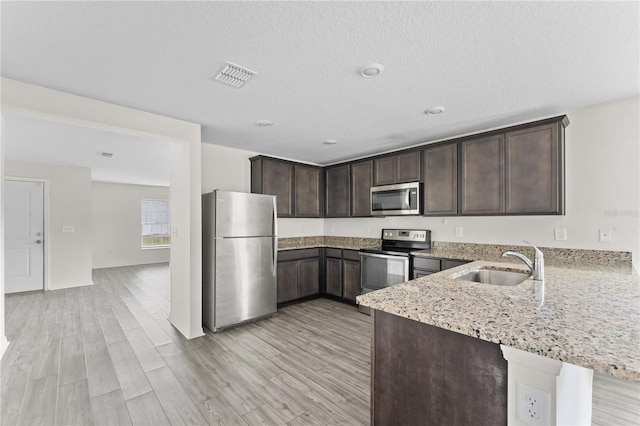 kitchen with sink, kitchen peninsula, stainless steel appliances, and light wood-type flooring