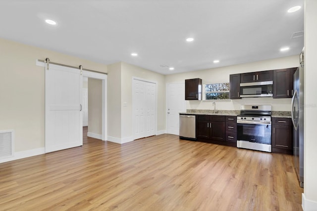 kitchen with sink, a barn door, light wood-type flooring, dark brown cabinetry, and stainless steel appliances