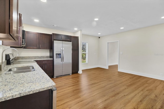 kitchen featuring light stone countertops, sink, stainless steel fridge with ice dispenser, dark brown cabinets, and light wood-type flooring