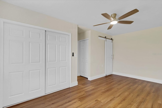 unfurnished bedroom featuring light wood-type flooring, a barn door, and ceiling fan