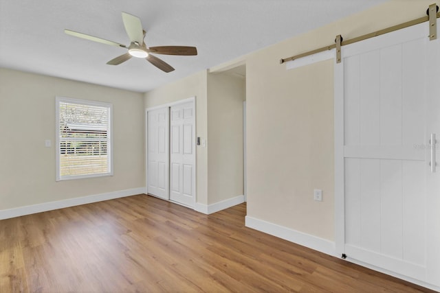 unfurnished bedroom with a barn door, ceiling fan, a closet, and light hardwood / wood-style floors