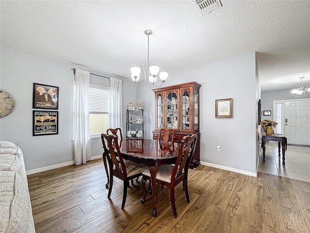 dining space featuring light hardwood / wood-style flooring, a textured ceiling, and an inviting chandelier