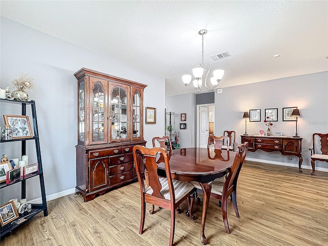 dining area featuring light wood-type flooring, a textured ceiling, and an inviting chandelier