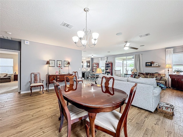 dining area with a textured ceiling, light hardwood / wood-style floors, and ceiling fan with notable chandelier