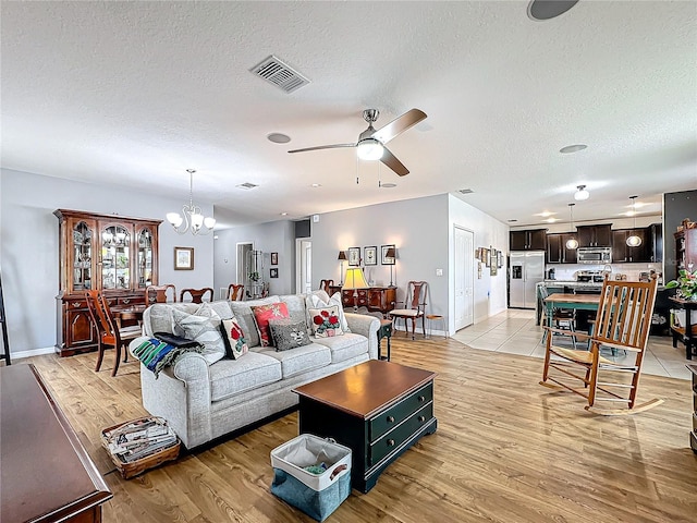 living room with ceiling fan with notable chandelier, a textured ceiling, and light wood-type flooring