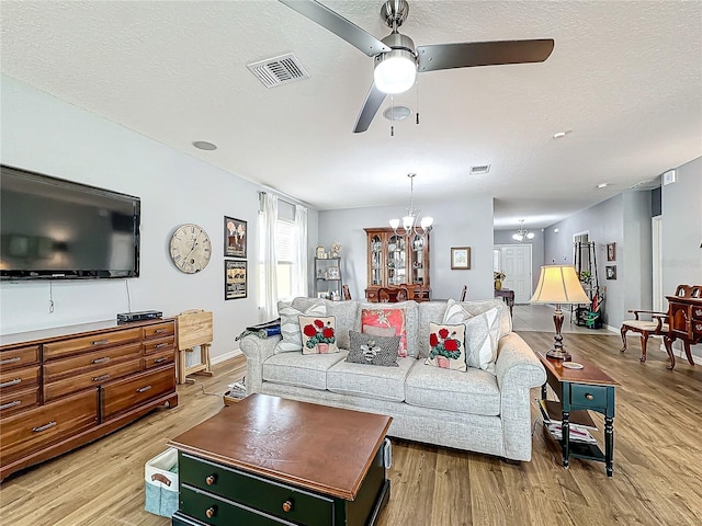 living room featuring ceiling fan with notable chandelier, a textured ceiling, and light hardwood / wood-style floors