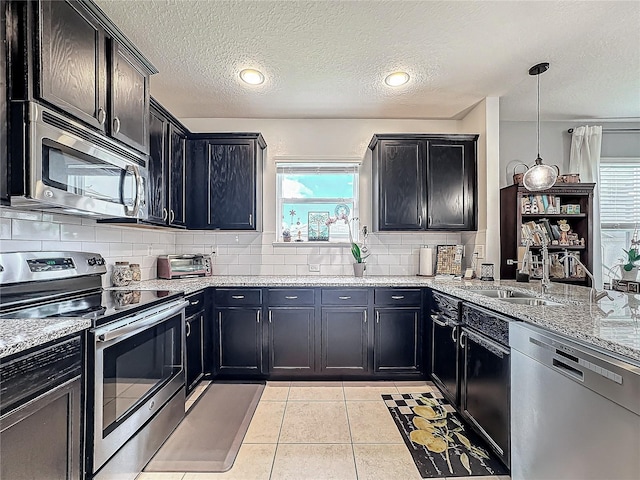 kitchen with sink, a textured ceiling, decorative light fixtures, light tile patterned flooring, and appliances with stainless steel finishes