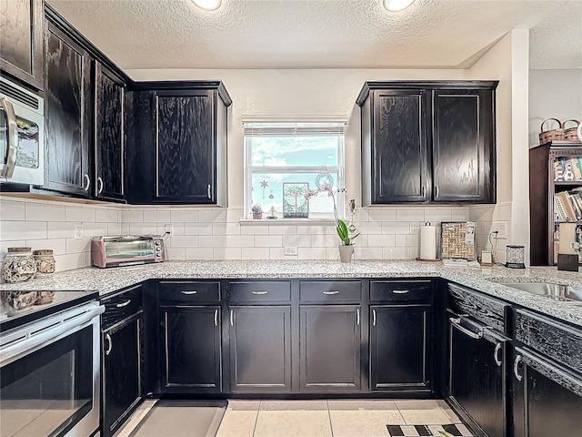 kitchen featuring backsplash, light tile patterned flooring, a textured ceiling, and appliances with stainless steel finishes