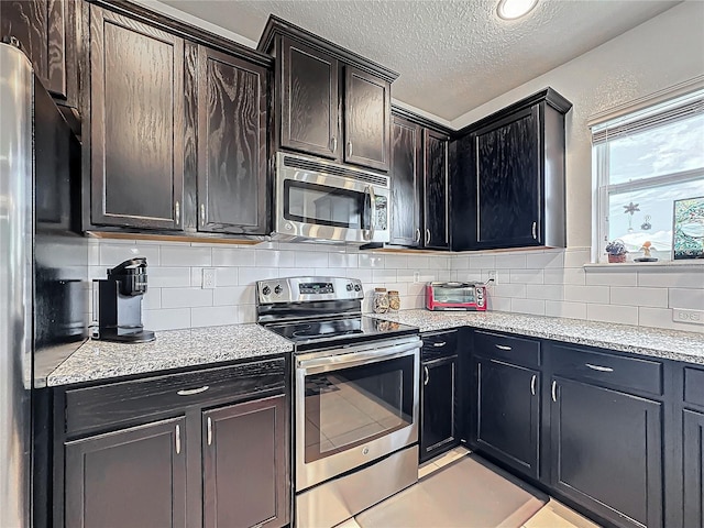 kitchen with light stone countertops, a textured ceiling, dark brown cabinets, light tile patterned floors, and appliances with stainless steel finishes