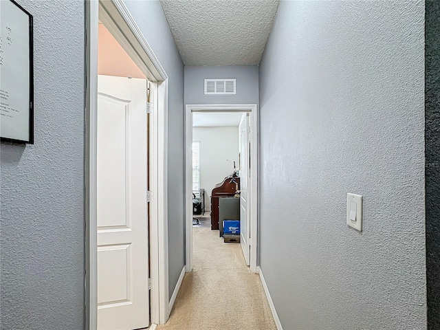 hall featuring light colored carpet and a textured ceiling