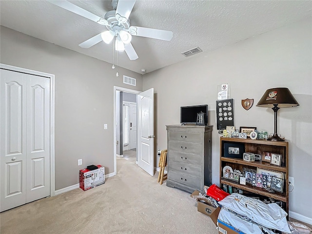 bedroom with a textured ceiling, a closet, ceiling fan, and light colored carpet