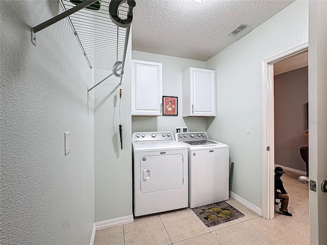 clothes washing area featuring light tile patterned floors, cabinets, a textured ceiling, and independent washer and dryer