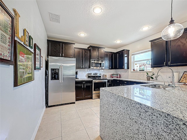 kitchen with sink, hanging light fixtures, stainless steel appliances, light stone counters, and decorative backsplash