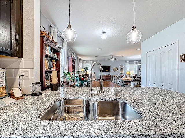 kitchen with sink, a textured ceiling, pendant lighting, ceiling fan, and light stone countertops