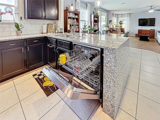 kitchen with light tile patterned floors, sink, backsplash, dark brown cabinetry, and light stone countertops