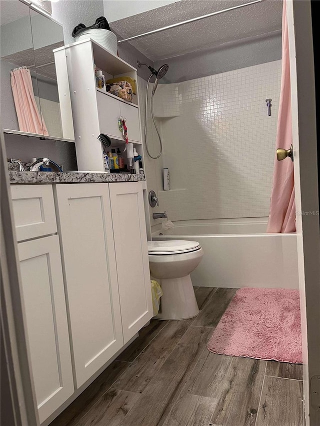 full bathroom with hardwood / wood-style floors, vanity, shower / bath combination with curtain, toilet, and a textured ceiling