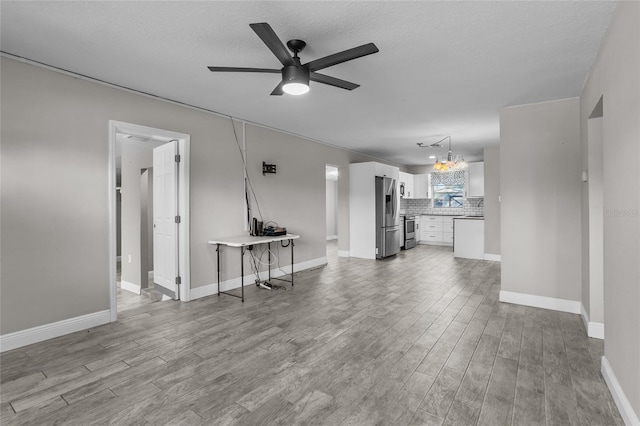 unfurnished living room with ceiling fan with notable chandelier, a textured ceiling, and light hardwood / wood-style flooring