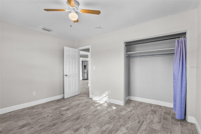 unfurnished bedroom featuring stainless steel fridge, ceiling fan, a closet, and light wood-type flooring