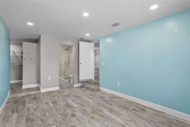 unfurnished bedroom featuring light hardwood / wood-style flooring, ensuite bath, and a spacious closet