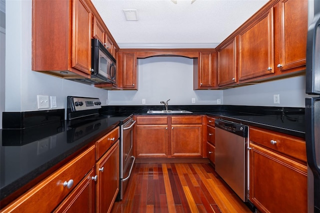 kitchen featuring dark stone counters, sink, a textured ceiling, dark hardwood / wood-style flooring, and stainless steel appliances