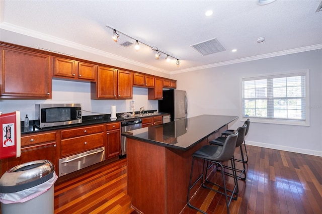 kitchen featuring a kitchen breakfast bar, dark hardwood / wood-style flooring, ornamental molding, a textured ceiling, and stainless steel appliances