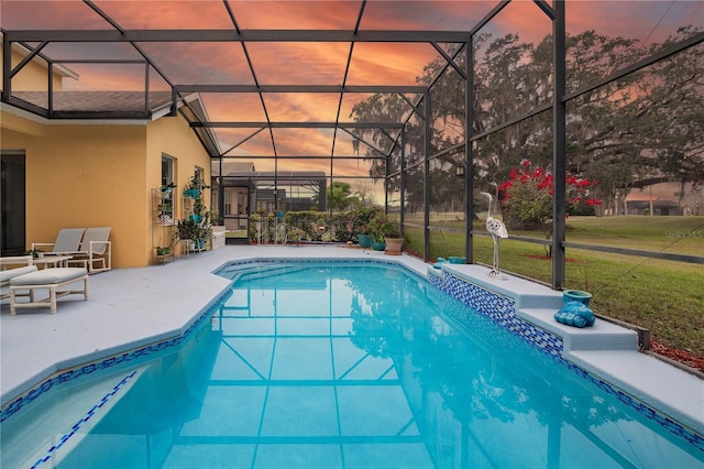 pool at dusk with a patio, glass enclosure, and a lawn