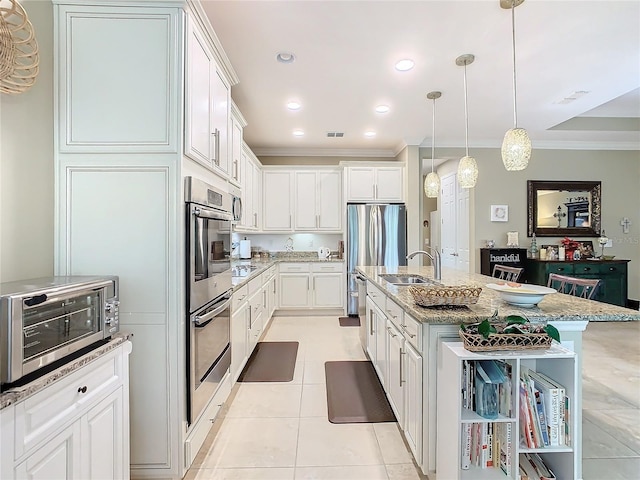 kitchen featuring light stone counters, sink, decorative light fixtures, white cabinets, and an island with sink