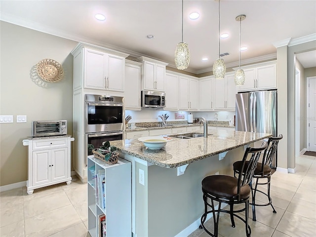 kitchen with light stone countertops, stainless steel appliances, sink, a center island with sink, and white cabinetry