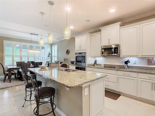 kitchen with light stone countertops, sink, stainless steel appliances, decorative light fixtures, and a center island with sink