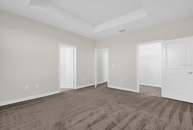 unfurnished bedroom with carpet, a tray ceiling, a spacious closet, and a closet