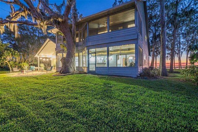 back house at dusk with a patio, a yard, and a sunroom