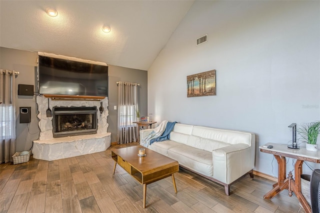 living room featuring a textured ceiling, vaulted ceiling, and a fireplace