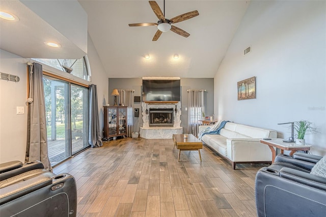 living room featuring ceiling fan, high vaulted ceiling, a fireplace, and hardwood / wood-style flooring