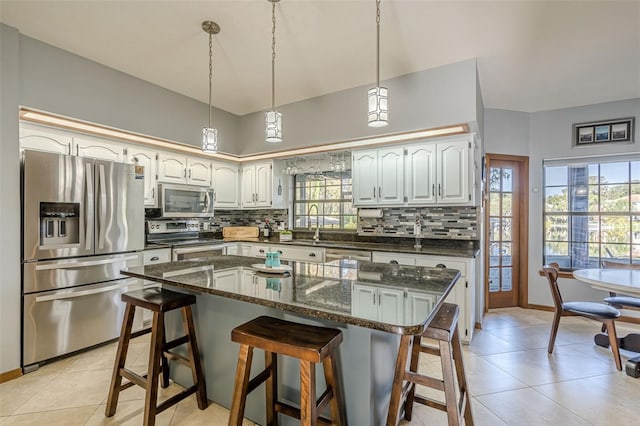 kitchen featuring appliances with stainless steel finishes, a center island, white cabinetry, dark stone counters, and a breakfast bar area