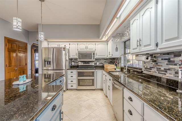 kitchen with white cabinets, appliances with stainless steel finishes, decorative light fixtures, dark stone counters, and sink