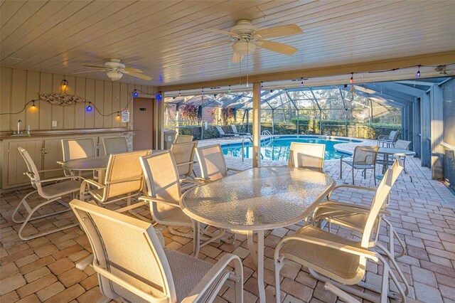 view of patio featuring ceiling fan, glass enclosure, area for grilling, and exterior bar