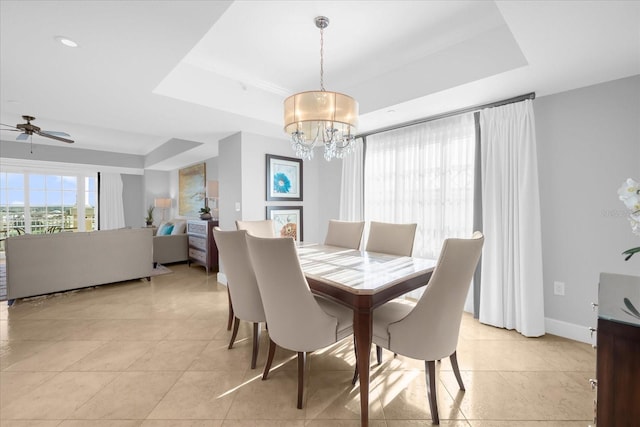 tiled dining room featuring ceiling fan with notable chandelier and a raised ceiling