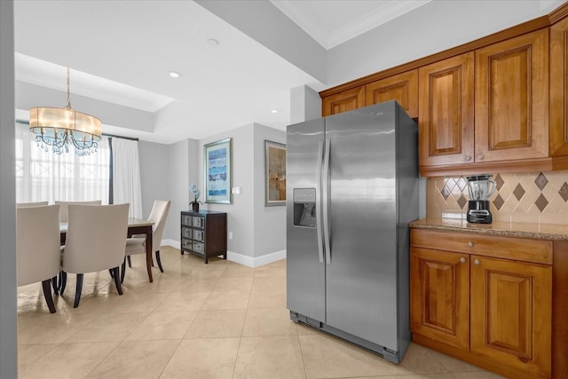 kitchen with hanging light fixtures, decorative backsplash, stainless steel fridge, light stone countertops, and a notable chandelier