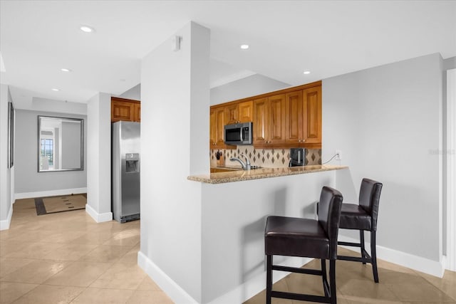 kitchen featuring decorative backsplash, light stone countertops, light tile patterned flooring, kitchen peninsula, and stainless steel appliances