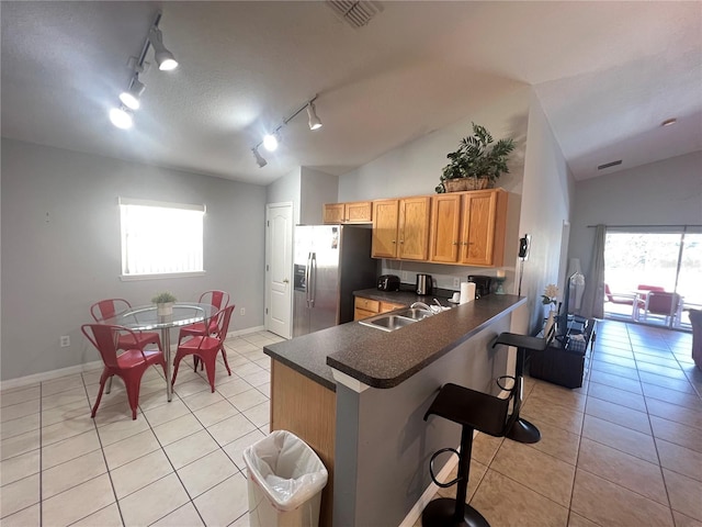 kitchen featuring track lighting, stainless steel refrigerator with ice dispenser, a breakfast bar, and vaulted ceiling