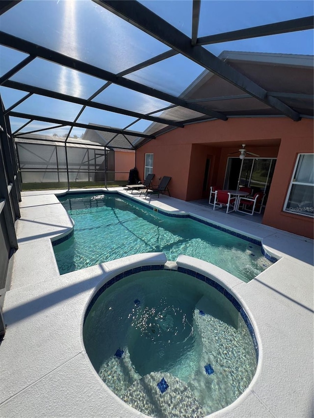 view of swimming pool with glass enclosure, ceiling fan, an in ground hot tub, and a patio