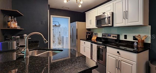 kitchen with stainless steel appliances, white cabinetry, dark stone countertops, and sink