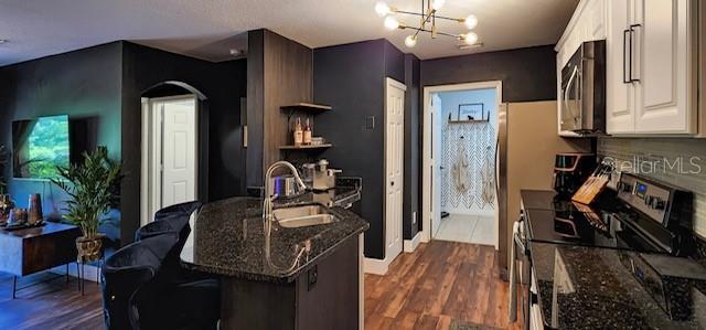 kitchen with black range with electric cooktop, dark wood-type flooring, sink, dark stone countertops, and white cabinetry