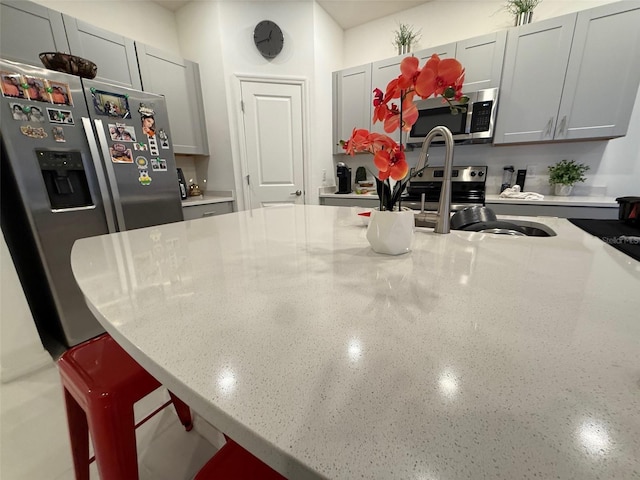 kitchen featuring a kitchen breakfast bar, gray cabinetry, light stone counters, and stainless steel appliances