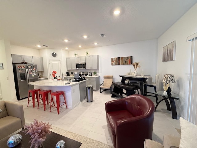 kitchen featuring gray cabinetry, a kitchen island with sink, a breakfast bar area, light tile patterned flooring, and stainless steel appliances