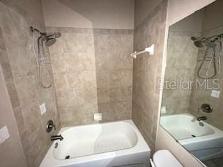 bathroom with tiled shower / bath combo and toilet