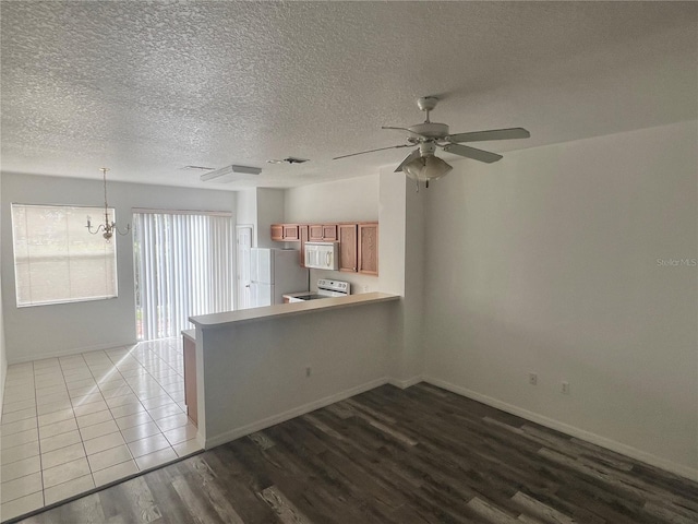 interior space featuring kitchen peninsula, wood-type flooring, decorative light fixtures, white appliances, and ceiling fan with notable chandelier