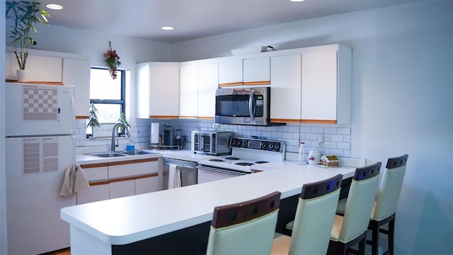 kitchen with sink, kitchen peninsula, decorative backsplash, appliances with stainless steel finishes, and white cabinetry