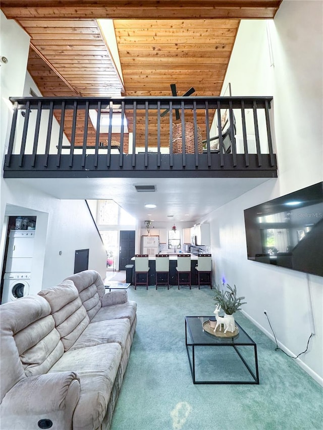 living room featuring stacked washer / dryer, a towering ceiling, carpet floors, and wood ceiling