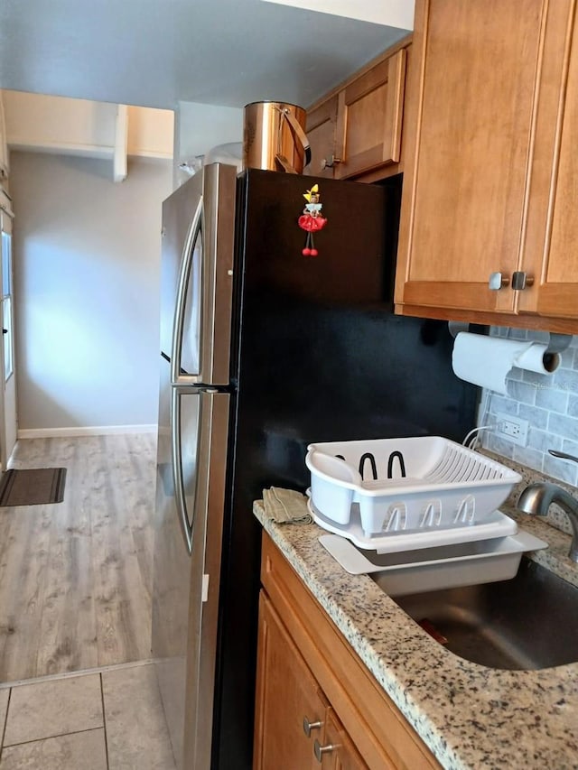 kitchen with stainless steel fridge, light stone countertops, and backsplash